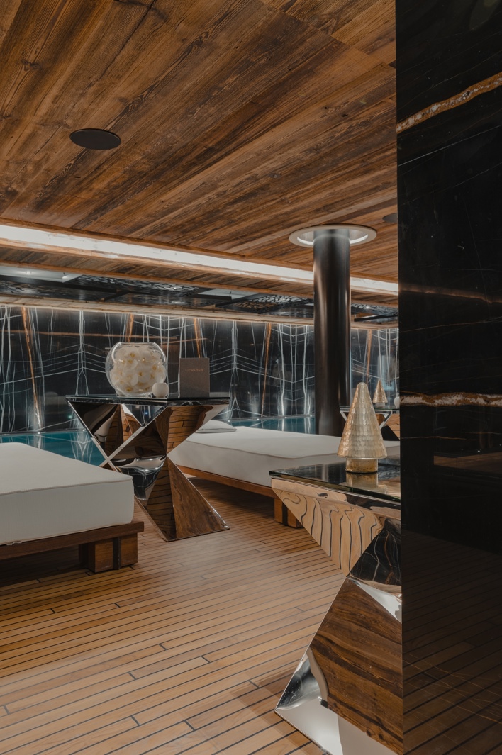 Luxurious spa relaxation area with modern wooden decor, marble accents, and poolside lounge beds illuminated by warm ambient lighting.