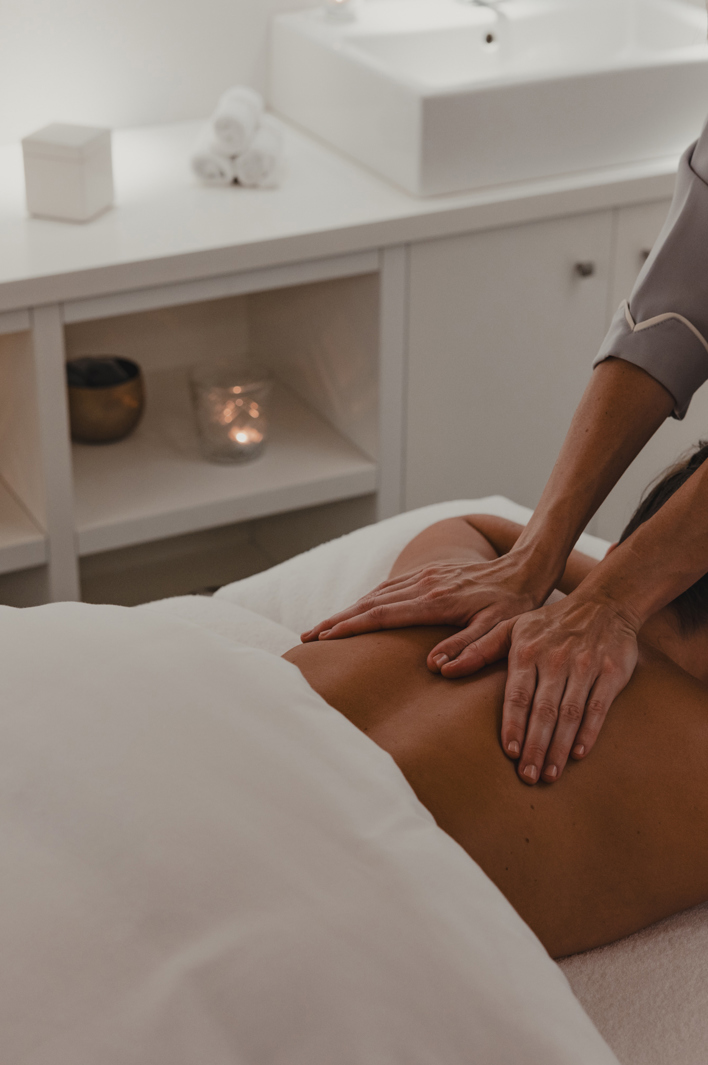 Therapist performing a relaxing back massage in a serene spa treatment room with soft lighting and candles.