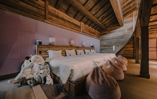 Family or children’s bedroom in a luxury alpine chalet with three twin beds, soft pink paneling, plush beanbags, and cuddly stuffed animals, offering a cozy mountain retreat for younger guests in a warm wooden interior.