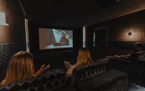 Elegant private home cinema with plush velvet seating, warm ambient lighting, and a large projection screen showing a movie.