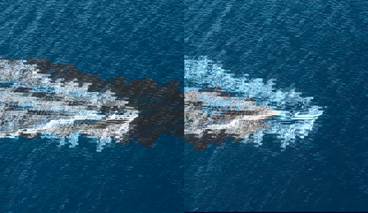 A motor yacht cruising at high speed across the deep blue sea, leaving a foamy white trail behind it.