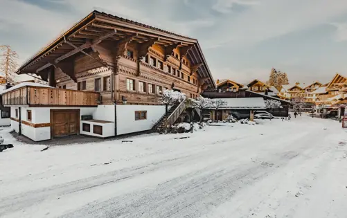 Traditional alpine chalet with carved wooden architecture in a snowy mountain village on a clear winter day.