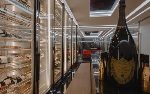 Elegant luxury wine cellar with illuminated glass wine racks, Dom Pérignon champagne bottles, and a red sports car displayed behind glass.