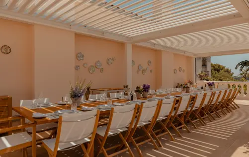 Elegant outdoor dining terrace with a long wooden table set for a large gathering under a modern pergola with soft natural light.