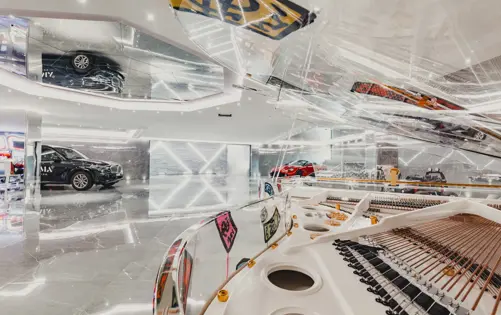 High-end luxury garage with polished marble floors, modern lighting, sports cars, and a transparent grand piano reflecting the contemporary design.