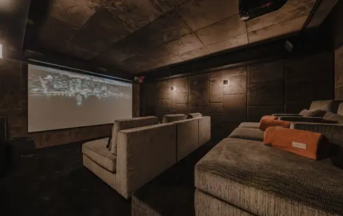 Private cinema room in a luxury alpine chalet with plush tiered seating, warm ambient lighting, and a large projection screen — offering an exclusive home theater experience in a mountain retreat.