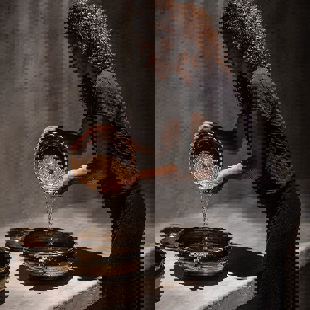 Spa therapist pouring water from a brass bowl into another during a traditional relaxation ritual.
