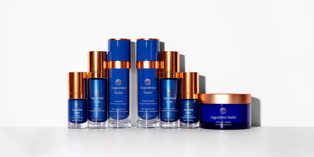 Collection of Augustinus Bader skincare products including The Cream, The Rich Cream, and The Body Cream in blue and copper packaging.