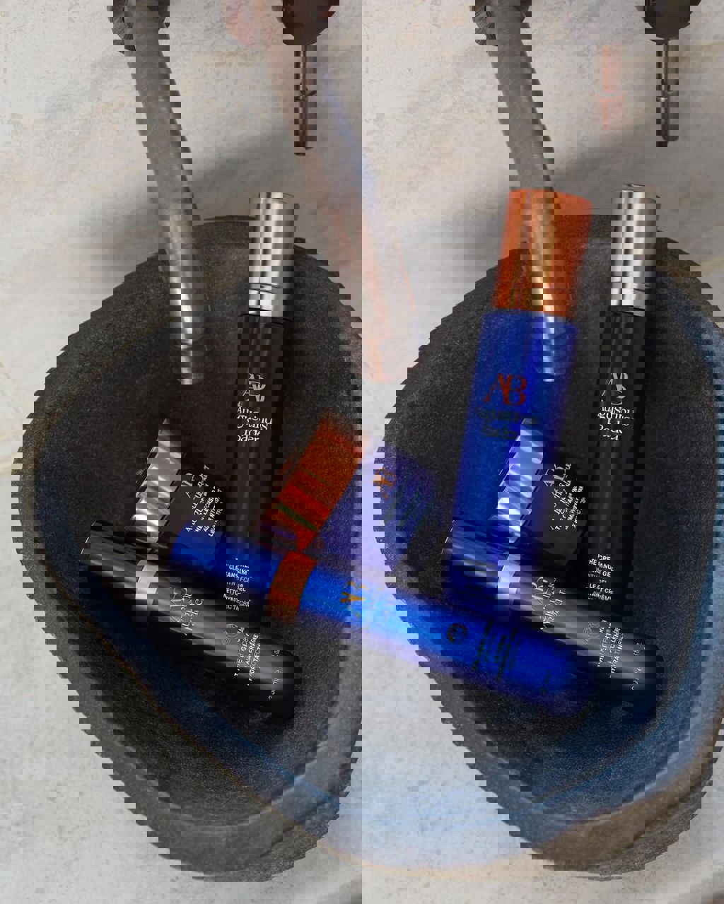 Augustinus Bader skincare products, including The Cream Cleansing Gel and The Light Cream, displayed in a stone sink under a metallic faucet.