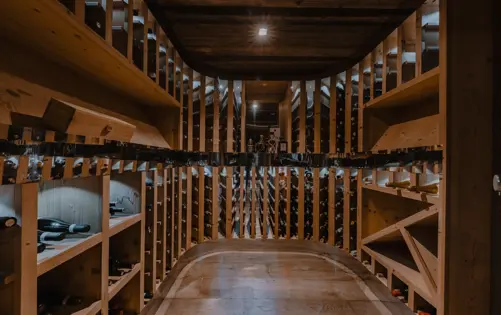Luxury chalet wine cellar with wooden shelves, soft lighting, and a collection of fine wines arranged in a temperature-controlled room.