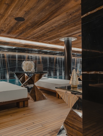 Luxurious spa relaxation area with modern wooden decor, marble accents, and poolside lounge beds illuminated by warm ambient lighting.