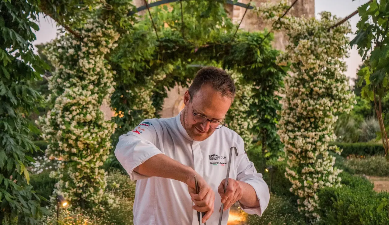 Gourmet chef preparing pasta in a wheel of cheese at an elegant outdoor dining setting.