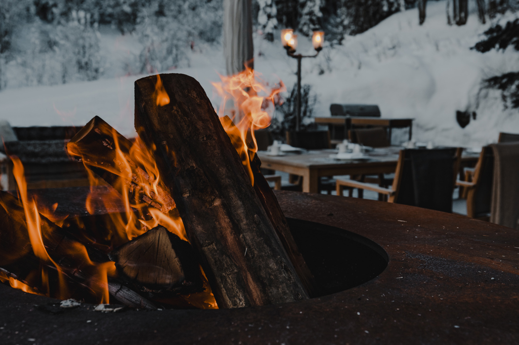 Warm outdoor fire pit with burning logs in a snowy mountain setting at dusk.