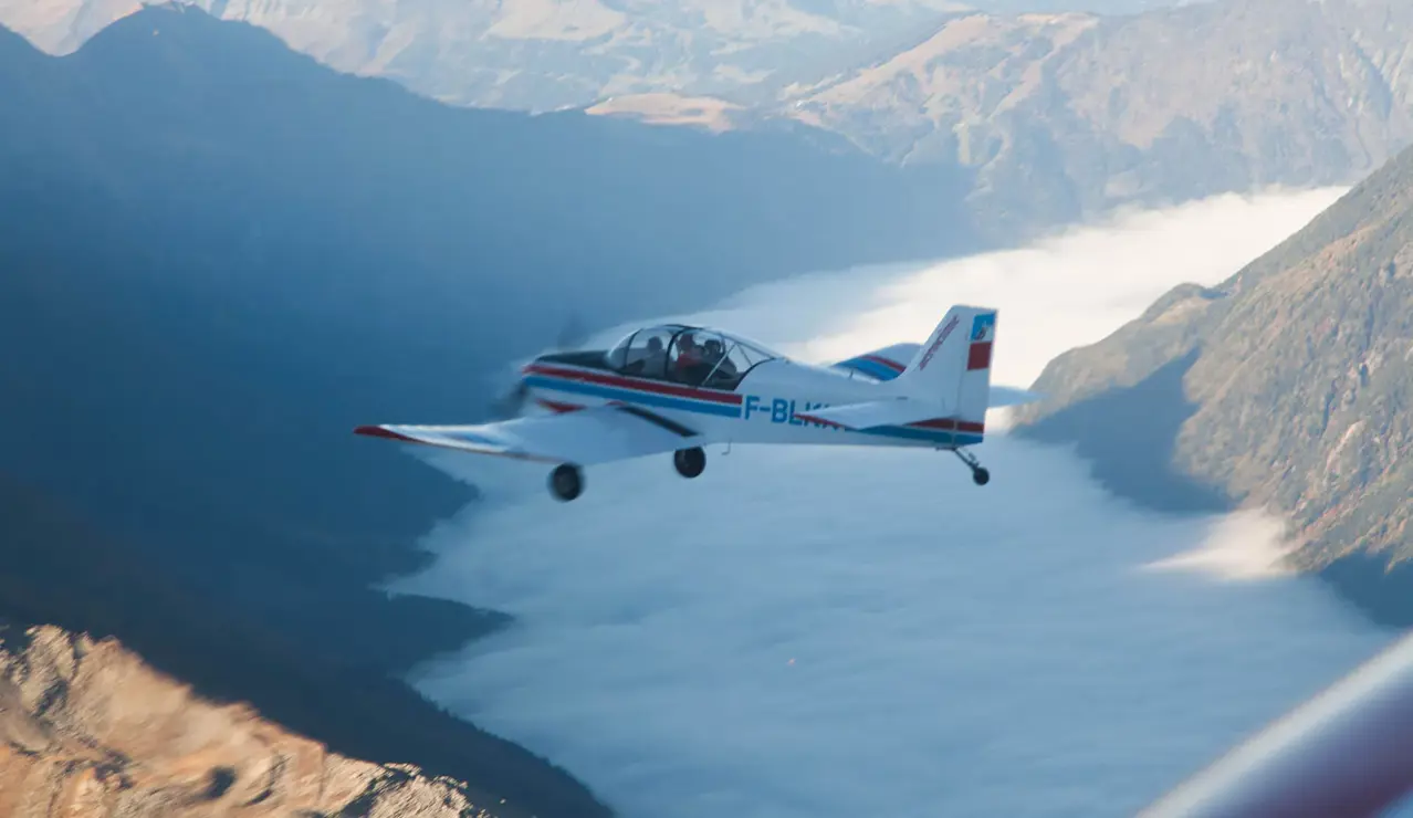 A small aircraft soars above a sea of clouds framed by rugged alpine peaks.