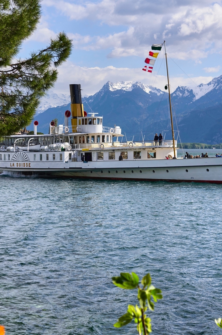 Elegant boat sailing on a tranquil lake, framed by flowers and mountains in the background.