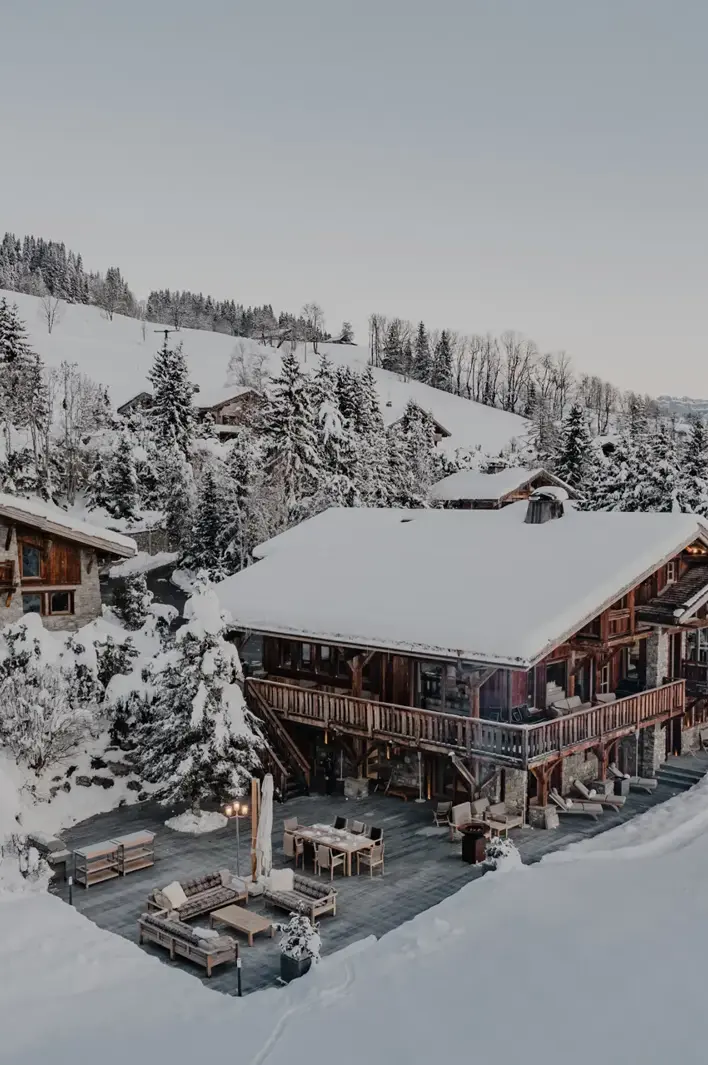Luxury alpine chalet surrounded by snow-covered trees and mountain views at dusk.