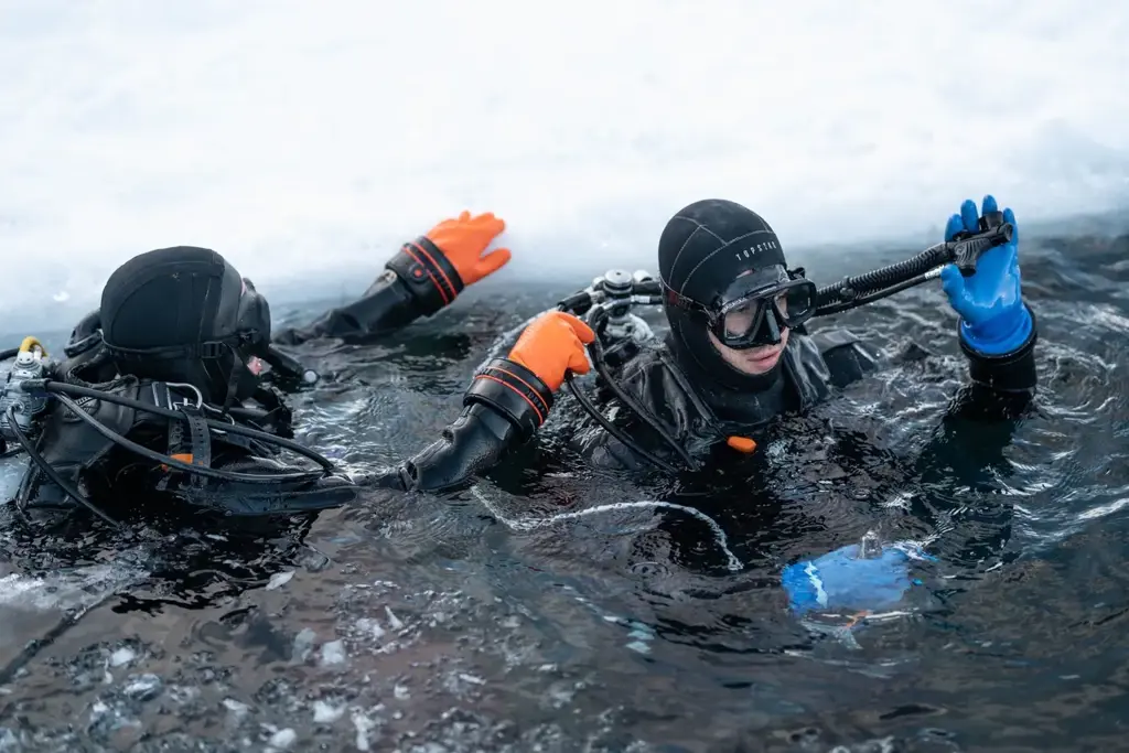 غواصان يرتديان معدات الغوص في المياه الباردة يظهران من فتحة جليدية، يتعاونان لاستكشاف الأعماق تحت سطح الجليد.