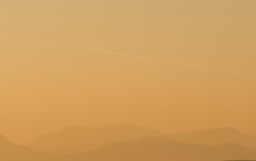 Serene coastal landscape with layered mountain silhouettes at sunset over calm sea.