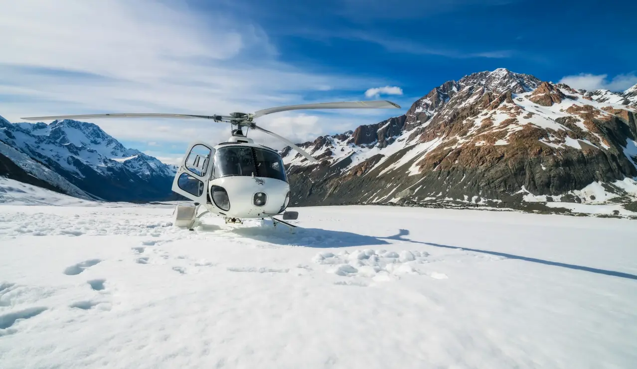 A helicopter rests on a pristine snowfield surrounded by rugged peaks and clear blue skies — the essence of alpine exploration.