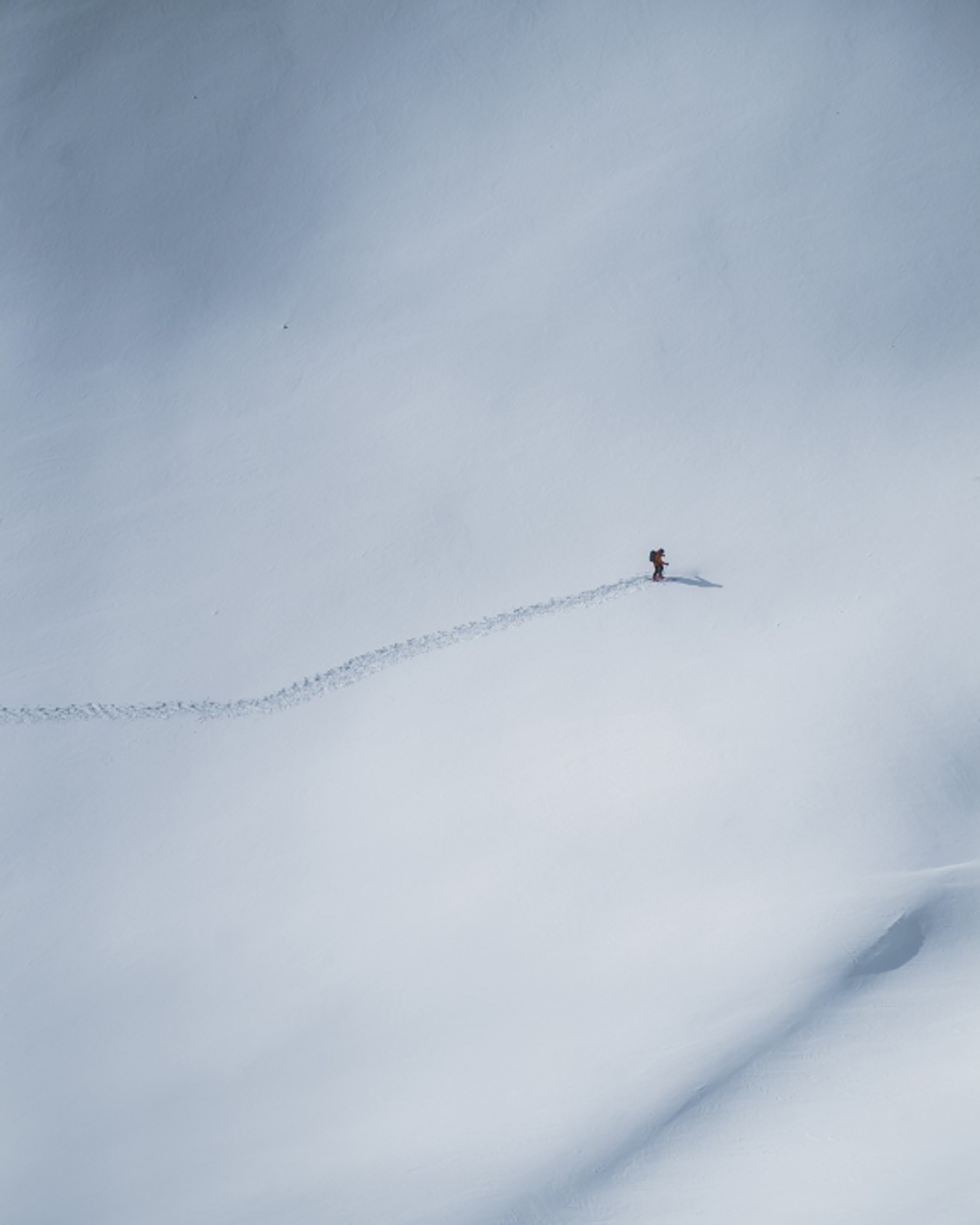 Solo skier making fresh tracks across untouched snow on a mountain slope.