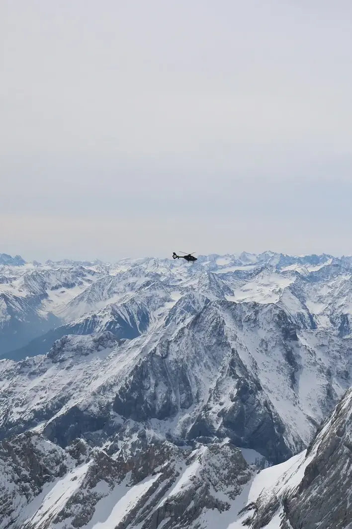 A helicopter flies above snow-covered alpine peaks on a clear winter day.