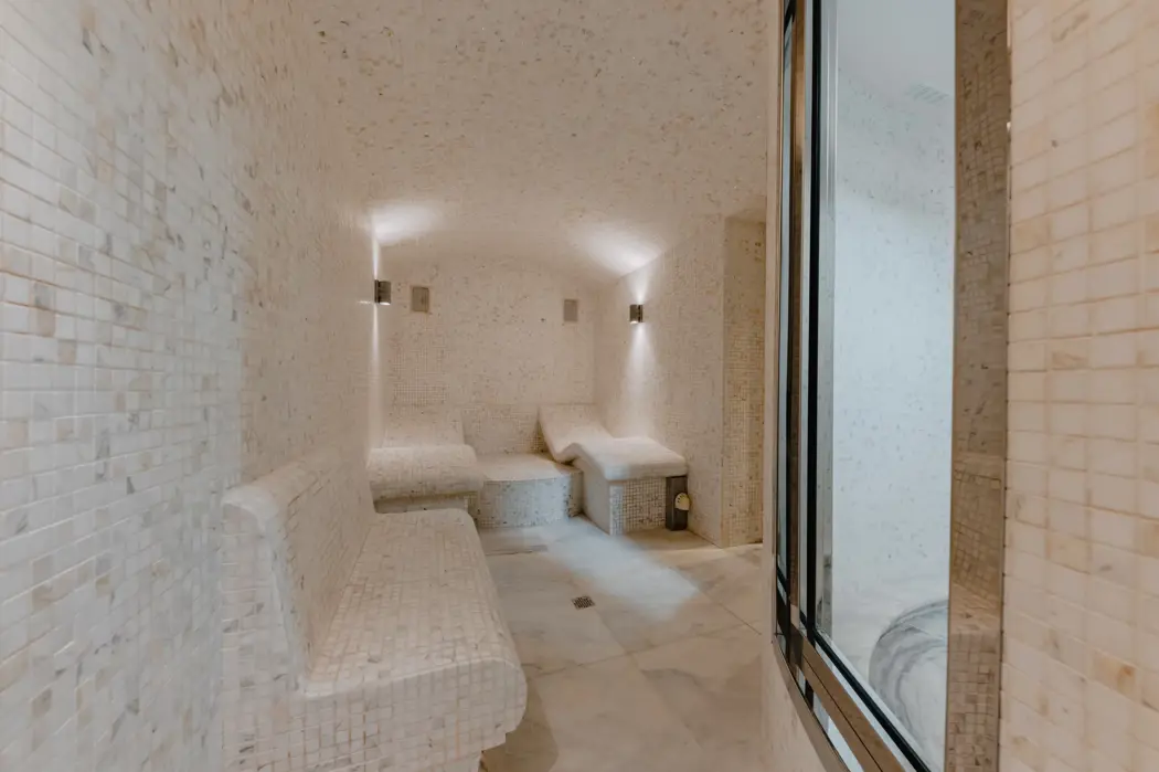 Luxurious spa steam room with marble mosaic tiles, curved heated benches, and soft lighting for a serene wellness experience.